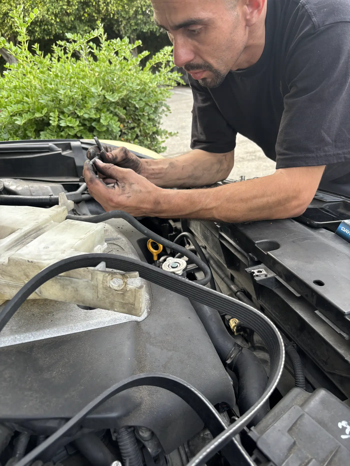 Hands working inside an open engine bay in daylight.